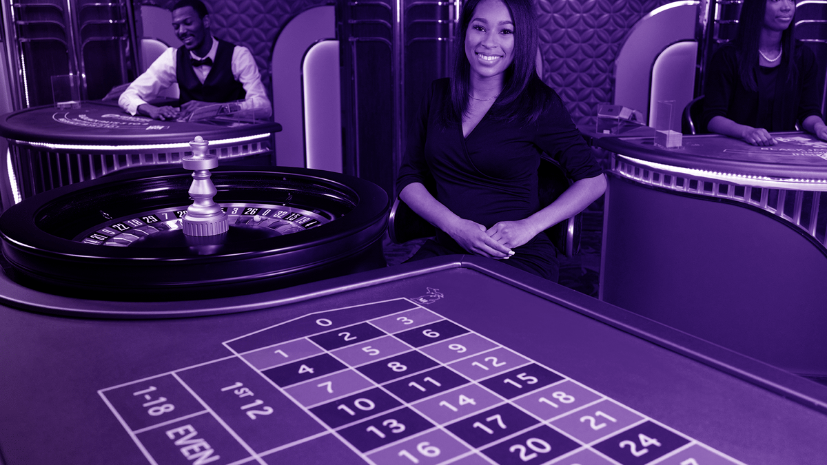 Leende dealer vid ett roulettebord i ett live casino, med andra dealers i bakgrunden.